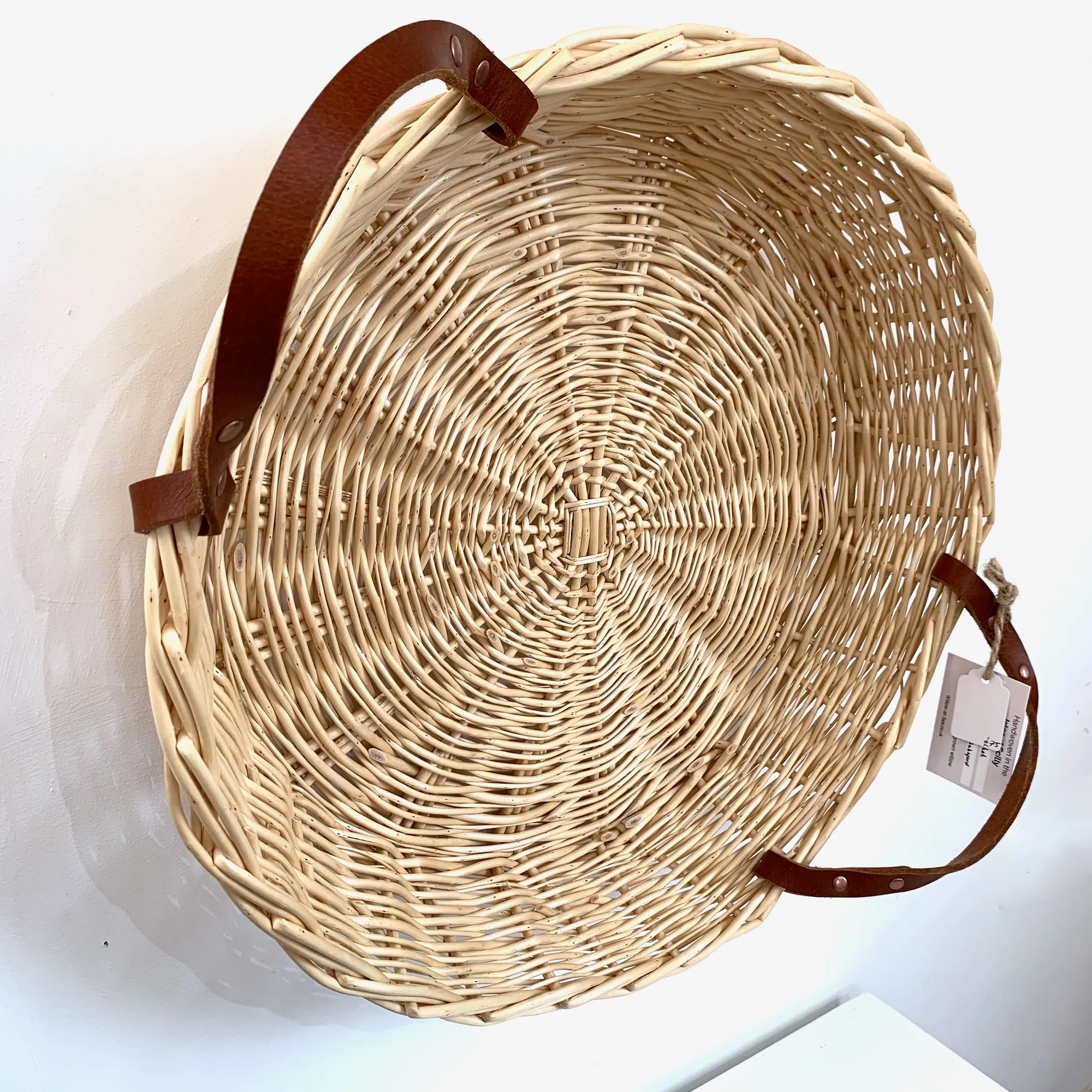 a shallow white willow basket with leather handles hung on a wall