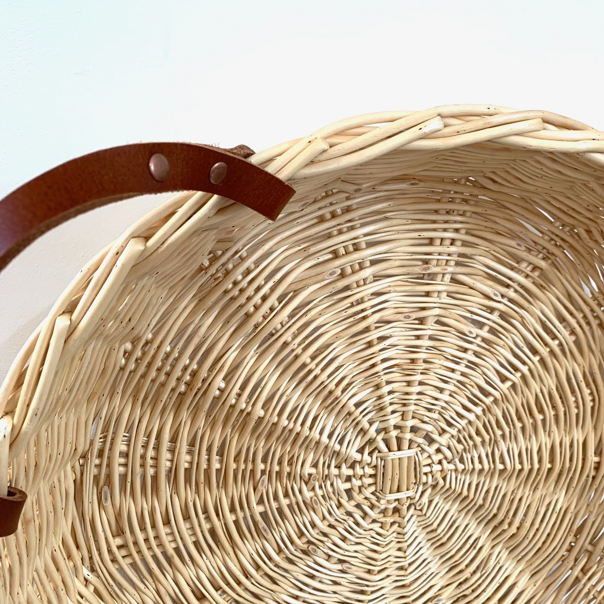 close up of a shallow white willow basket with leather handles