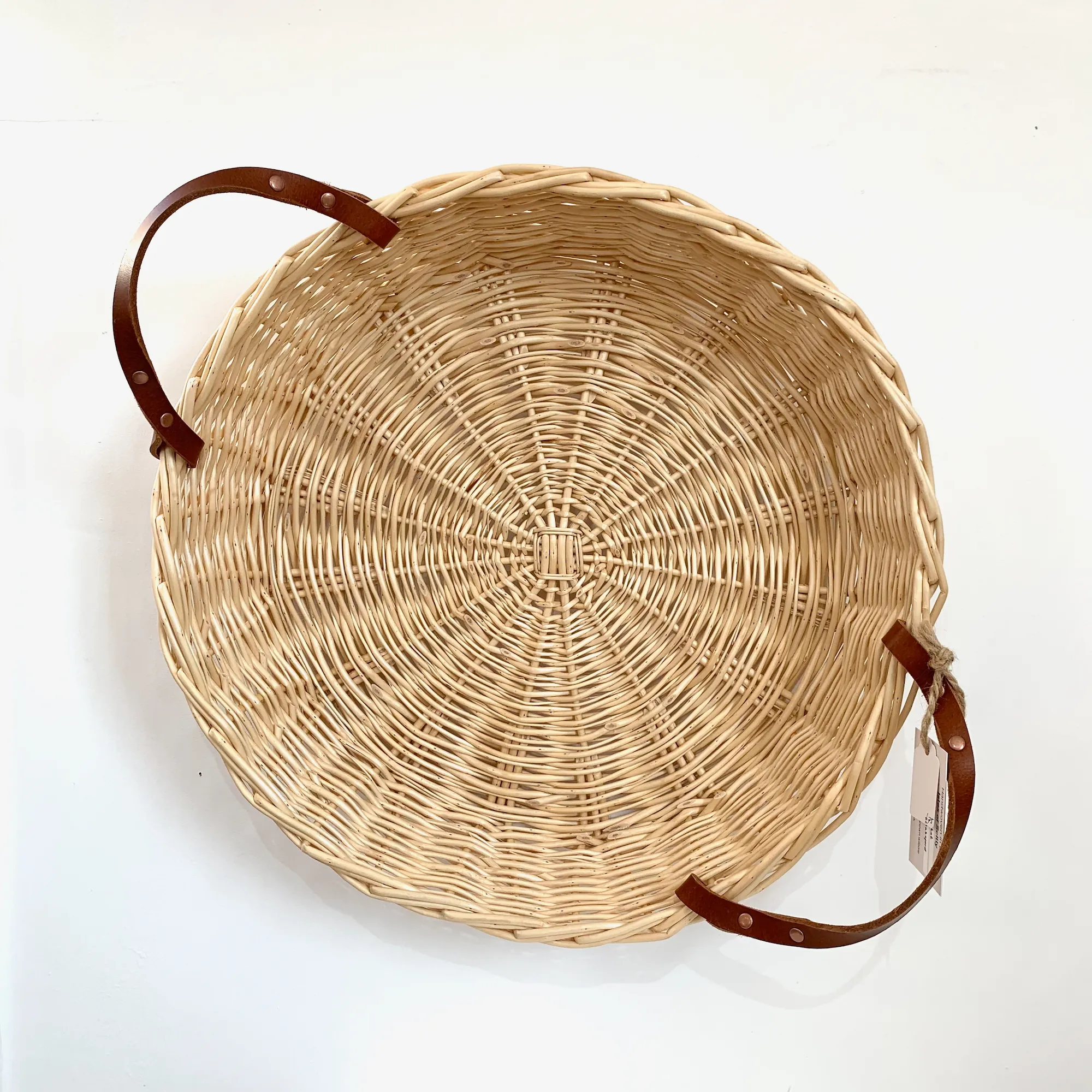 a shallow white willow basket with leather handles hung on a wall