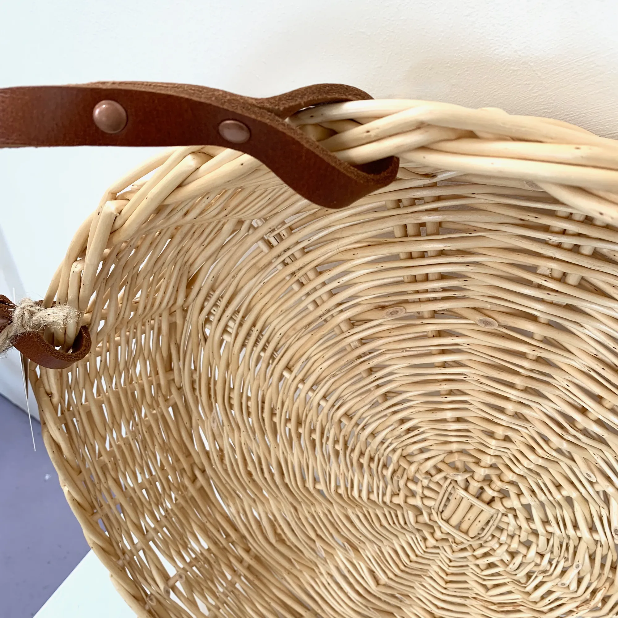 a close up showing the handle of a shallow white willow basket with leather handles
